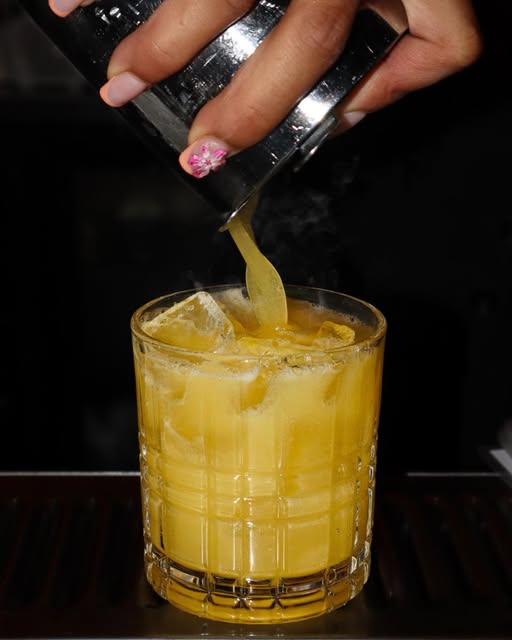 A cocktail being poured over ice at the bar