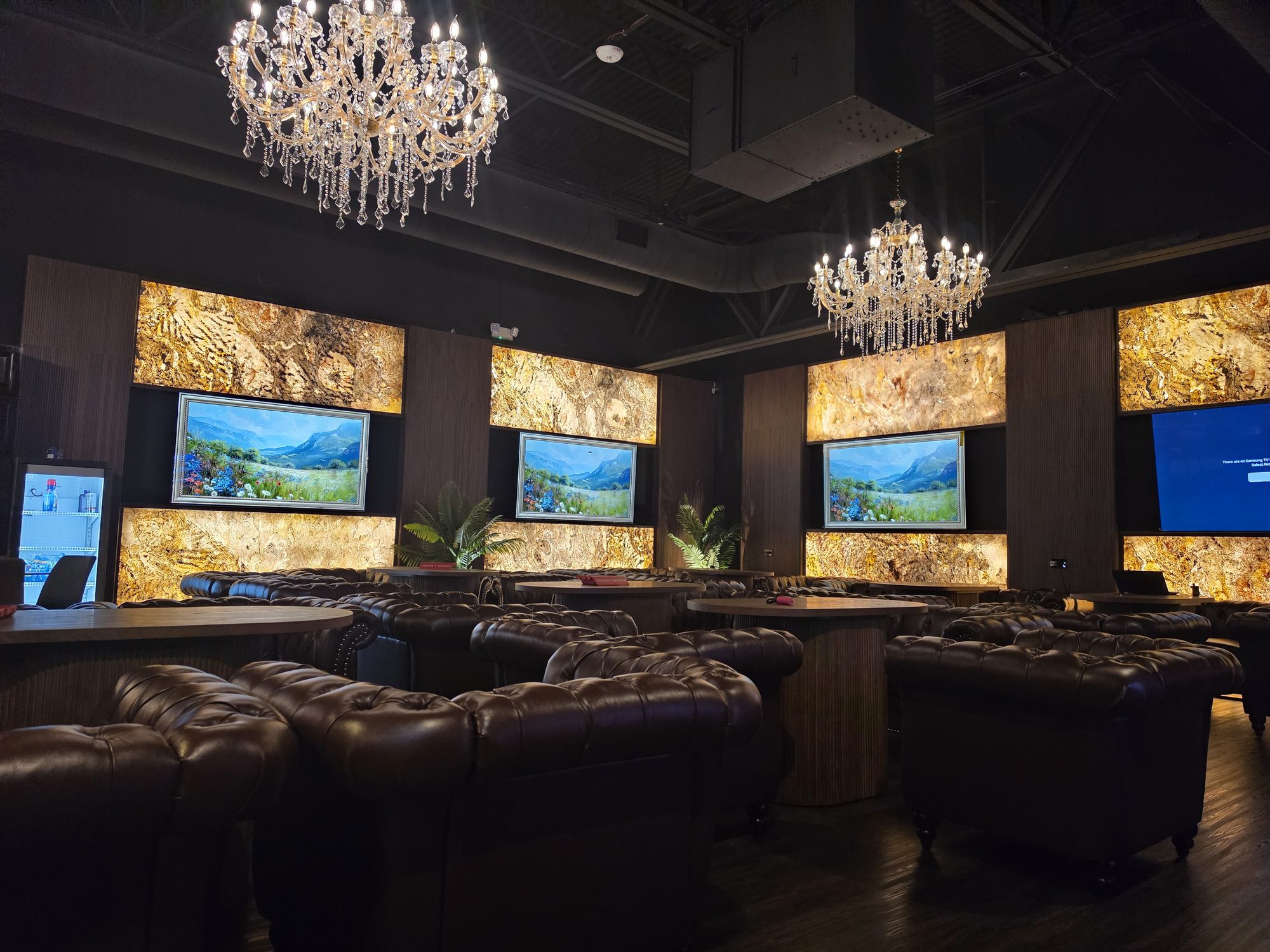 The private members' area at Cheroots Katy — leather chesterfields, backlit onyx walls and crystal chandeliers